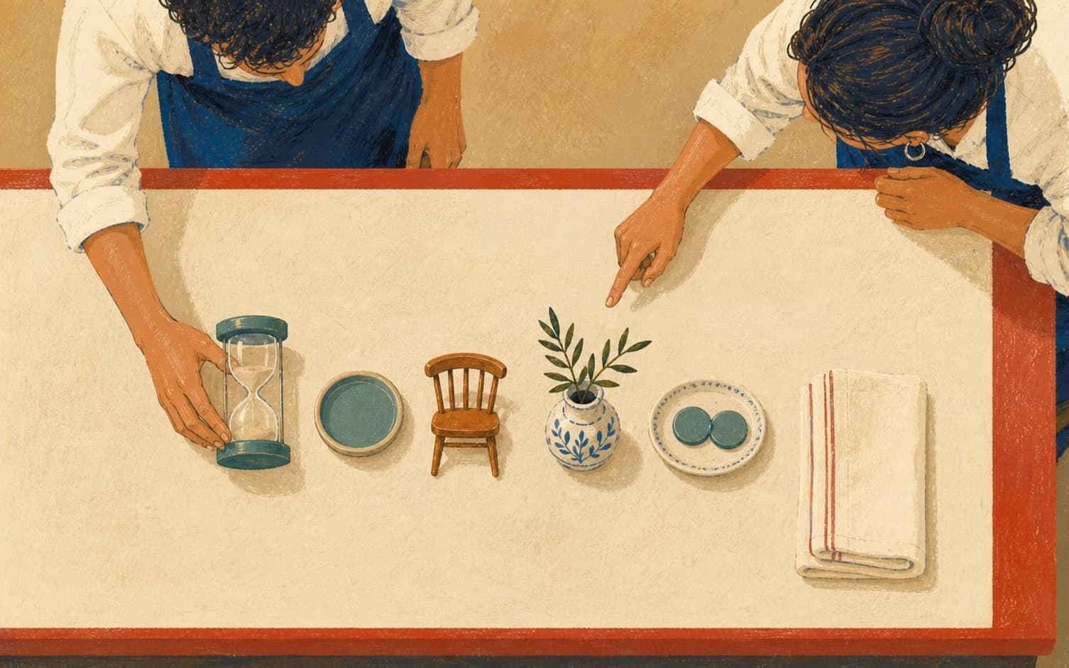 Two aproned staff lean over a red-edged counter arranging an hourglass, a tiny chair, a sprig-filled vase and a small plate along the table