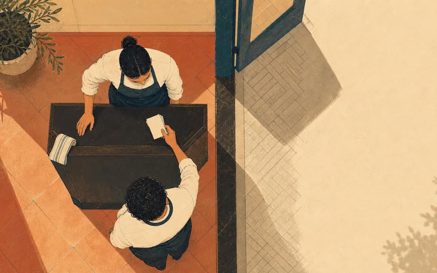 Seen from above, two aproned staff members meet at a dark table near an open doorway, one holding a small notepad while the other rests a hand on the table